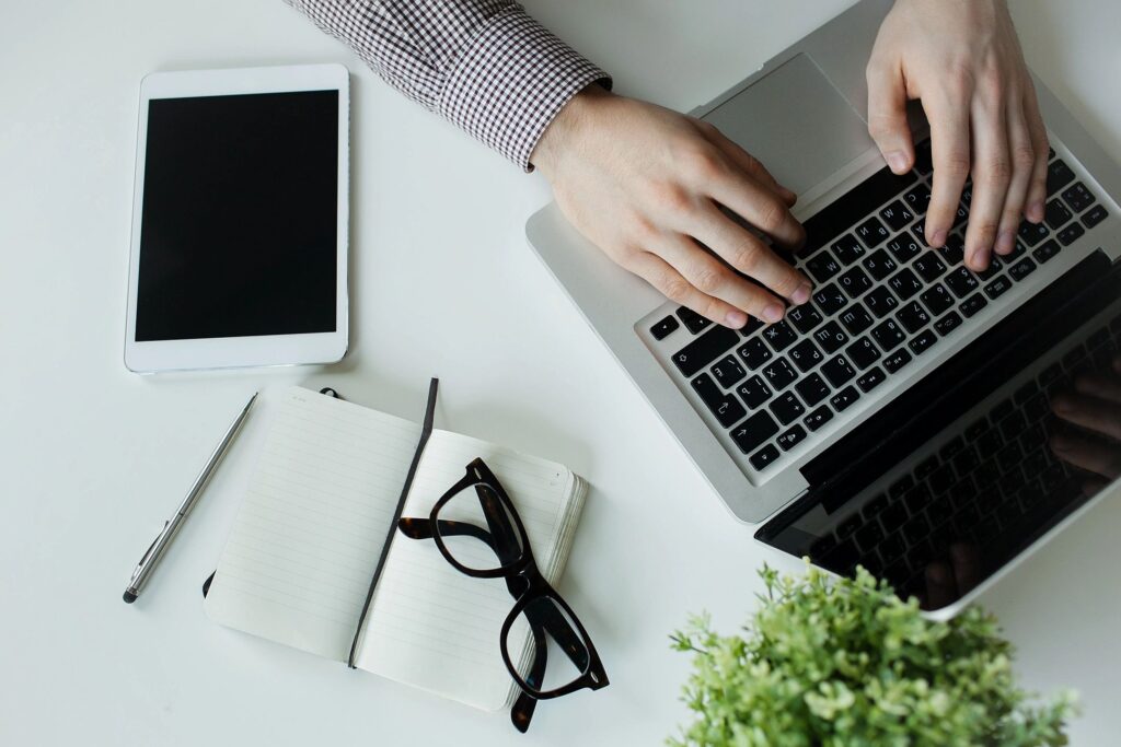 Someone typing on a computer next to an Ipad